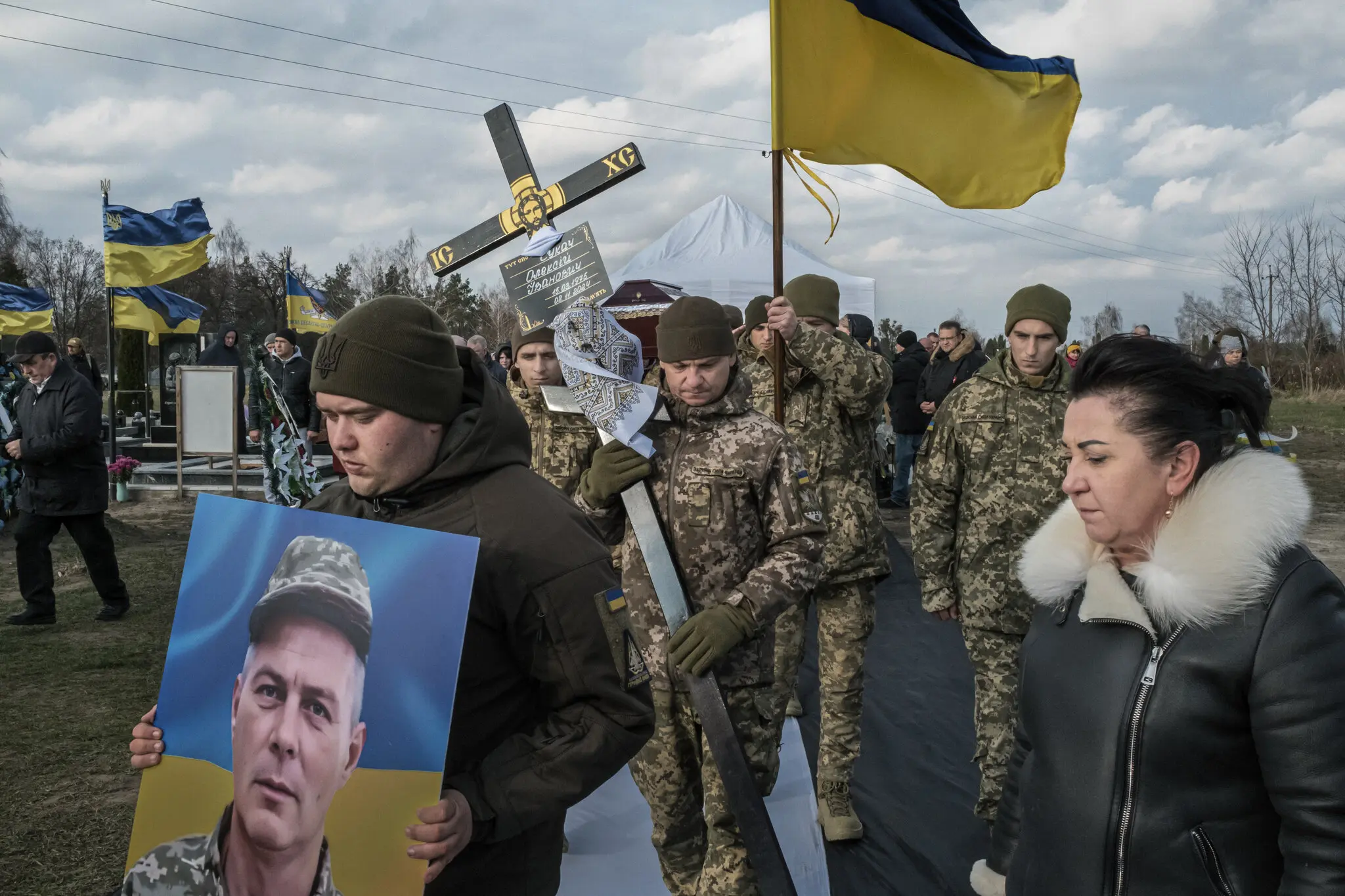 Український воїн несе фотографію свого побратима, поки його труну несуть до могили.
